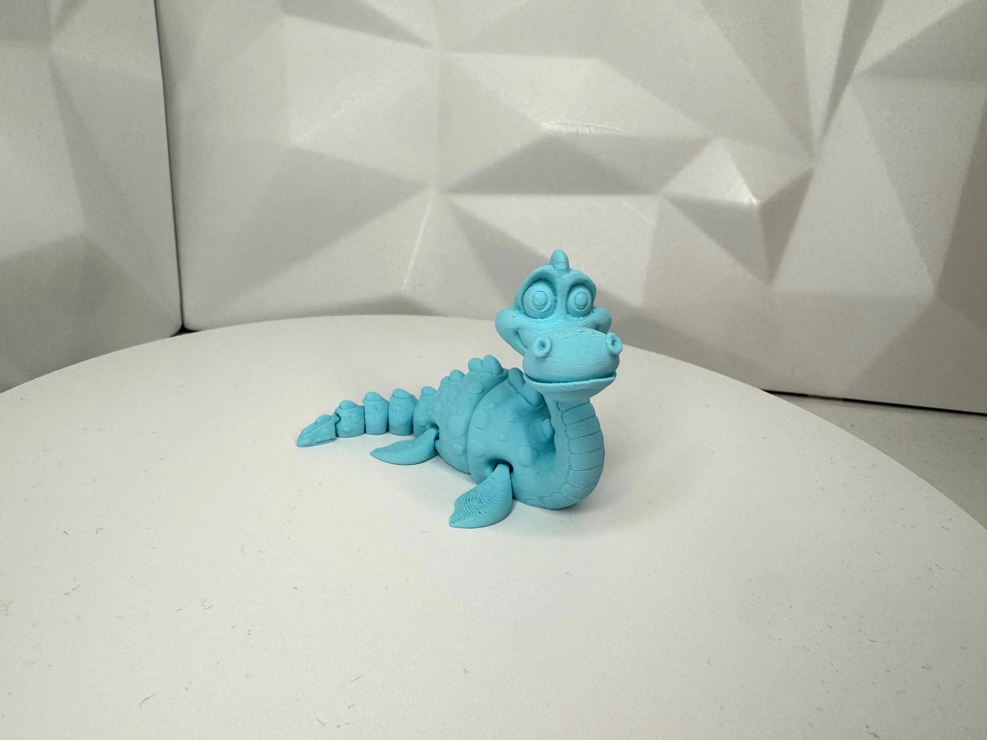 Hellblaue 3d-gedruckte Nessie-Figur in aufrechter Pose vorne, klein, Kopf beweglich, segmentierter Körper